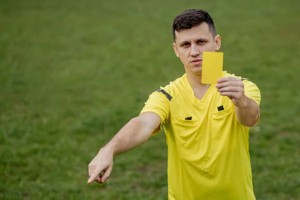 Angry football referee showing a yellow card and pointing with his hand on penalty.