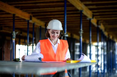 Mimar ya da mühendis, bina inşaatı projesini bina içinde ayrıntılı bir planla inceliyor. Kadın inşaat mühendisleri veya mimarlar çalışan insanlar.