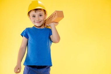 İnşaat kasklı çocuk elinde sarı arka planda bir tuğla tutuyor..