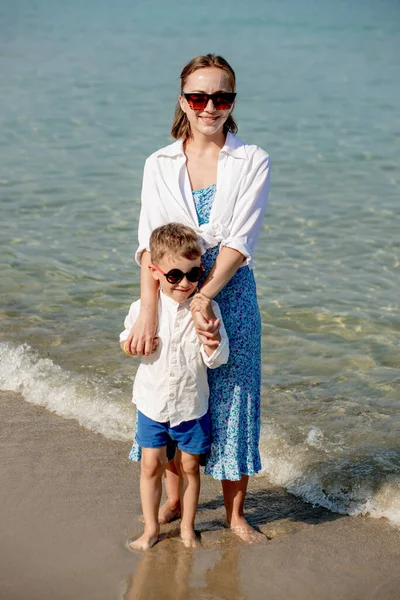 在海上阳光灿烂的日子里 快乐的年轻妈妈和儿子在一起 在海滩上休息 幸福的家庭 — 图库照片