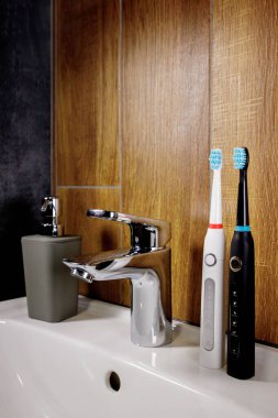 Banyodaki lavaboda iki elektrikli diş fırçası ve gri bir sabun makinesi. Krom kaplama musluk ve lavabo. Banyo içi ve aksesuar konsepti.