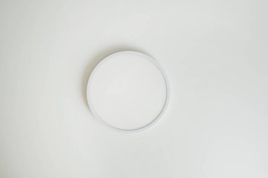Yuvarlak, minimalist, beyaz tavanda basit bir lamba. Dikkat çekmeyen bir lamba.