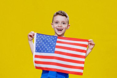 Sarı arka planda Amerikan bayrağı tutan gülümseyen küçük çocuk. Vatanseverlik, bağımsızlık günü, bayrak günü konsepti. Anma Günü.