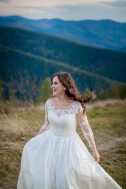 Güzel bir düğün çifti, gelin ve damat, dağların arka planında aşıklar. Güzel takım elbiseli damat ve beyaz lüks elbiseli gelin. Düğün çifti yürüyor..
