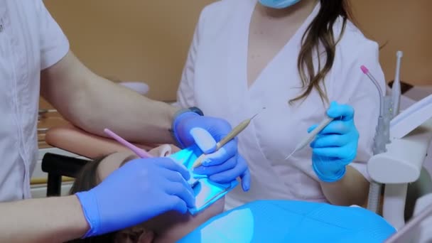 Дантист лечит женские зубы с помощью коффердама. Стоматологическое оборудование — стоковое видео