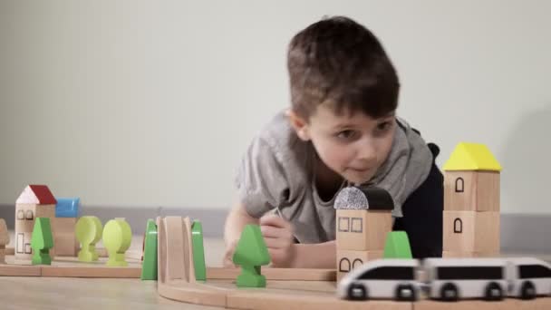 Leuke jongen speelt met een houten trein, neemt hem mee over de brug op vluchten. Houten educatief speelgoed — Stockvideo