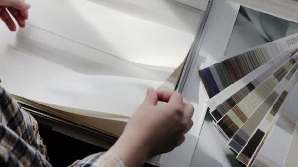 Mujer hojeando el catálogo con persianas enrollables o pantalla de ventana. Sistema de rodillo de ventana Duo día y noche. Elección de persianas enrollables — Vídeos de Stock