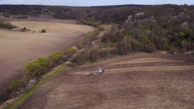 Havadan bakıldığında büyük bir traktör kuru bir alan oluşturuyor. Yukarıdan aşağıya traktör, toprağı işliyor ve kuru bir tarla ekiyor. Hava traktörü, tarla ekimi için çayırları kesiyor