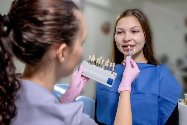 The dentist is trying to choose the right color for the teeth implants for the beautiful woman. — Stock Photo, Image
