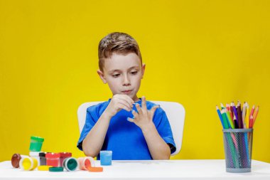 Küçük bir anaokulu öğrencisi elinde fırçayla masada oturur ve avucunu boyar. Anaokulu geliştirme