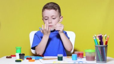 Küçük bir anaokulu öğrencisi elinde fırçayla masada oturur ve avucunu boyar. Anaokulu geliştirme.