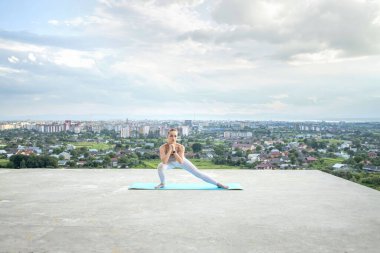 Genç bir kadın çatıda tek başına çalışıyor. Güzel bir şehir manzarası ve mavi gökyüzü.