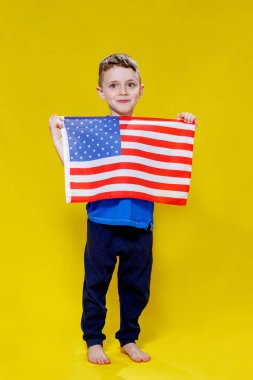 Sarı arka planda Amerikan bayrağı tutan gülümseyen küçük çocuk. Vatanseverlik, bağımsızlık günü, bayrak günü konsepti. Anma Günü.