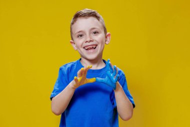 Avuç içleri sarı ve maviye boyanmış, Ukrayna bayrağı renginde küçük mutlu bir çocuk. Ukraynalı yaratıcı anaokulu öğrencisi.