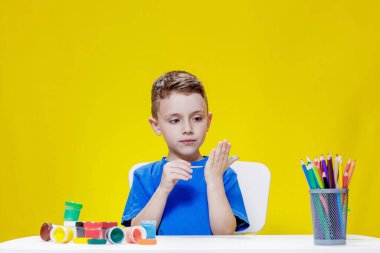 Küçük bir anaokulu öğrencisi elinde fırçayla masada oturur ve avucunu boyar. Anaokulu geliştirme