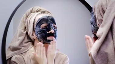 Genç bir kadın banyoda maske takıyor ve gülümsüyor. Güzel bir kadın aynanın önünde güzellik tedavisi yapıyor..