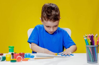 Küçük bir anaokulu öğrencisi masada oturuyor, avuç içlerini bir kağıt parçasına çiziyor. Renkli el izleri. Anaokulu geliştirme.