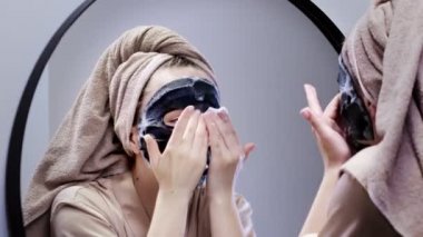 Genç bir kadın banyoda maske takıyor ve gülümsüyor. Güzel bir kadın aynanın önünde güzellik tedavisi yapıyor..