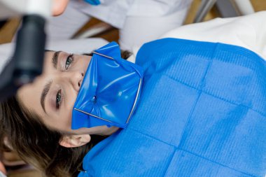 Bir dişçi, bir kadının dişlerini kabartma barajı kullanarak tedavi eder. Diş ekipmanları.