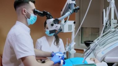 Mikroskop altında asistanı olan dişçi hastanın dişlerini tedavi ediyor. Modern ilerici dişçilik