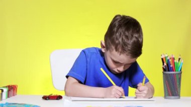 Çocuk masaya oturur ve renkli kalemlerle resim çizer. Yaratıcı çocuk. Anaokulu öğrencisi çiziyor. Okul öncesi geliştirme.