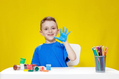 Küçük bir anaokulu öğrencisi masada oturuyor, avuç içlerini bir kağıt parçasına çiziyor. Renkli el izleri. Anaokulu geliştirme.