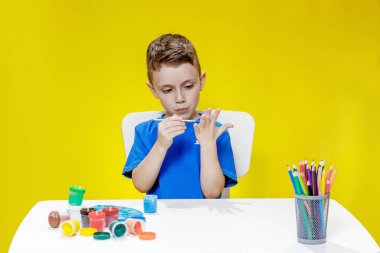 Küçük bir anaokulu öğrencisi elinde fırçayla masada oturur ve avucunu boyar. Anaokulu geliştirme
