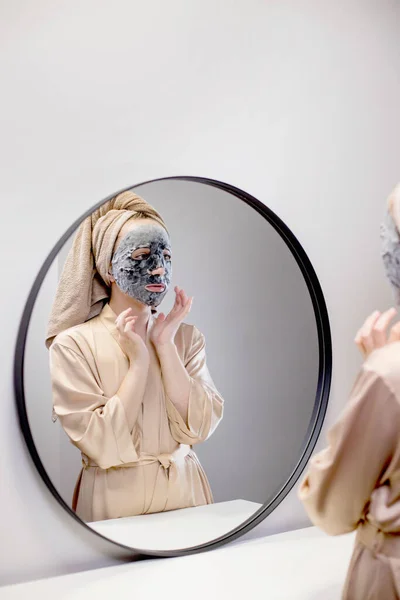 수건을 여성은 욕실에서 마스크를 만들고 거울을 여자는 피부를 이하기 — 스톡 사진