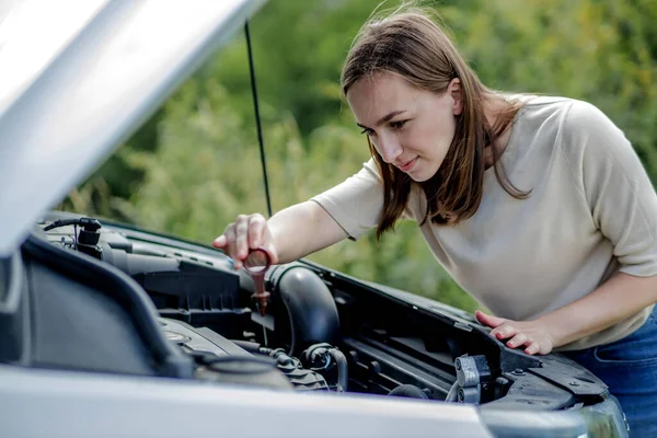 Kadın yağ seviyesini kontrol etmek için arabasının motoruna sonda yerleştiriyor. Kadın arabayı tek başına idare ediyor..