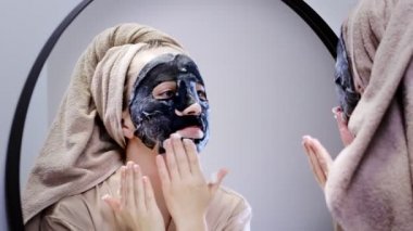 Genç bir kadın banyoda maske takıyor ve gülümsüyor. Güzel bir kadın aynanın önünde güzellik tedavisi yapıyor.