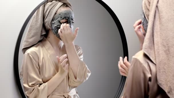 Młoda Szczęśliwa Kobieta Ręczniku Maska Twarzy Patrząc Lustrze Stylowej Łazience — Wideo stockowe
