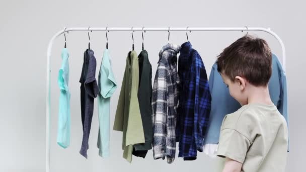 Menino Pré Escolar Junto Aos Cabides Acumula Roupas Escolhe Roupas — Vídeo de Stock