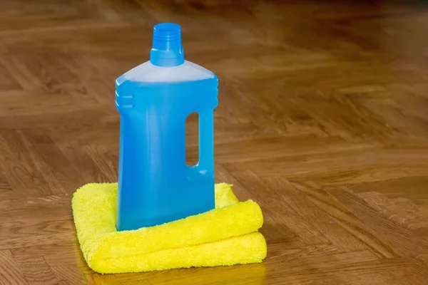 Floor cleaner in a plastic bottle and a floor cloth on the parquet floor indoors. House cleaning.