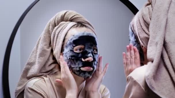 Młoda Szczęśliwa Kobieta Ręczniku Maska Twarzy Patrząc Lustrze Stylowej Łazience — Wideo stockowe