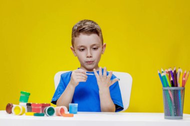 Küçük bir anaokulu öğrencisi elinde fırçayla masada oturur ve avucunu boyar. Anaokulu geliştirme