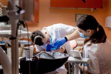 Bir dişçi, bir kadının dişlerini kabartma barajı kullanarak tedavi eder. Diş ekipmanları.