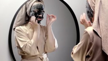 Evde bornoz ve havlu giymiş bakımlı bir kadın şişlik ve morluklardan dolayı gözlerinin altına bant yapıştırıyor. Kozmetik işlemler yapar - göz altı yamaları uygular.