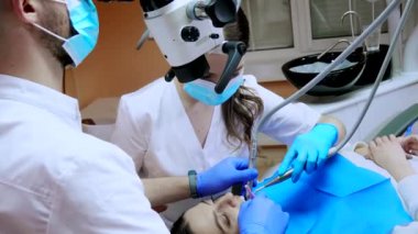 Mikroskop altında asistanı olan dişçi hastanın dişlerini tedavi ediyor. Modern ilerici dişçilik.