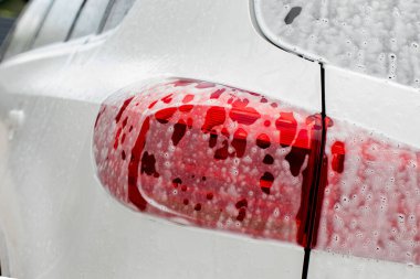 Araba farı yıkama. Su kaplı beyaz bir arabanın arka manzarası, çamaşır köpüğü ve kaput ve tamponda sabun. Profesyonel araba temizliği ve ticari temizlik kavramı..