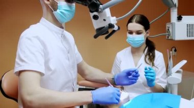 Mikroskop altında asistanı olan dişçi hastanın dişlerini tedavi ediyor. Modern ilerici dişçilik.