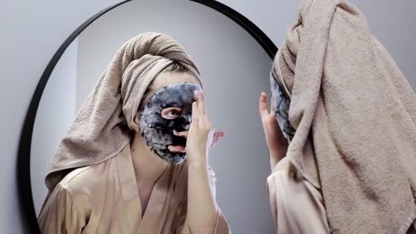 年轻快乐的女人戴着毛巾 做着面具 在时尚的浴室里照镜子 这个女人用面具来清洁皮肤 皮肤护理 — 图库视频影像