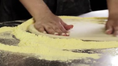 Bir pizzacı un kaplı bir yüzey üzerindeki hamuru şekillendirir ve geleneksel bir pizzacı mutfağında elle yoğurur.