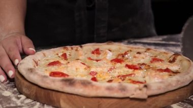 Freshly baked appetizing pizza with salmon and cherry tomatoes, cuting to slices with a pizza cutter for serving in a restaurant.