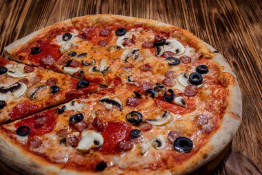 Tomato-based pizza with mozzarella cheese, hunting sausages, salami, olives, mushroom sauce. On a wooden background.