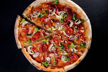 Vegan pizza with tomato sauce, cherry tomatoes, mushrooms, broccoli, red onion on black background. View from above.