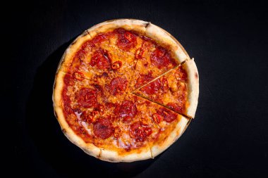 Pizza with tomato sauce, mozzarella, salami, chili, honey on black background. View from above.
