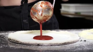 The chef prepares a delicious traditional Italian pizza and spreads tomato sauce on the round dough with an iron ladle. Cooking pizza.