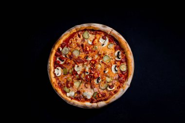 Appetizing pizza with hunting sausages, mozzarella cheese, pickled cucumbers, chili peppers on a tomato base. Mexican pizza. Top view.