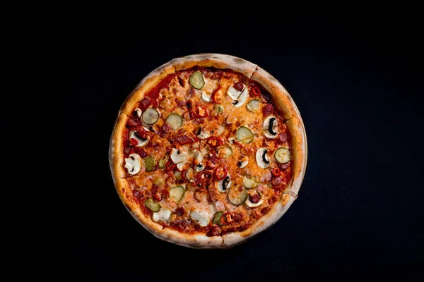 Appetizing pizza with hunting sausages, mozzarella cheese, pickled cucumbers, chili peppers on a tomato base. Mexican pizza. Top view.