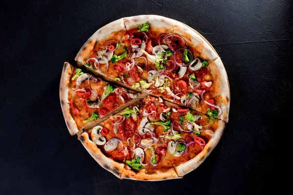 Vegan pizza with tomato sauce, cherry tomatoes, mushrooms, broccoli, red onion on black background. View from above.